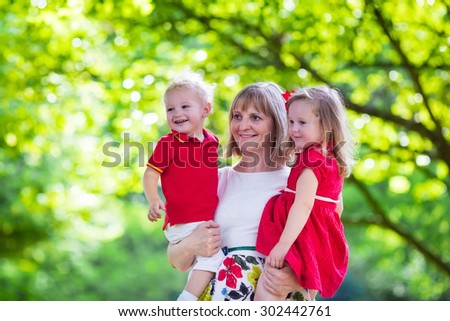 Mother and children play in a park. Woman holding little toddler daughter and son. Siblings with little age difference. Boy and girl twins. Young grandmother with grandchildren in sunny summer garden.