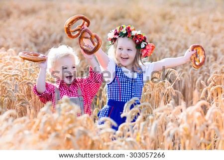 Kids in traditional Bavarian costumes in wheat field. German children eating bread and pretzel during Oktoberfest in Munich. Brother and sister play outdoors during autumn harvest time in Germany.
