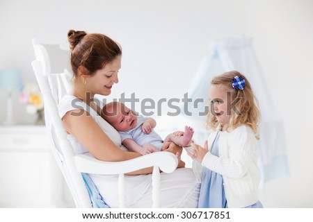 Little sister hugging her newborn brother. Toddler kid meeting new sibling. Mother and new born baby boy relax in a white bedroom. Family with children at home. Love, trust and tenderness concept.