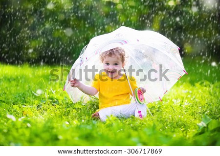 Little girl with colorful umbrella playing in the rain. Kids play outdoors by rainy weather in fall. Autumn outdoor fun for children. Toddler kid outside in the garden. Baby enjoying summer shower.