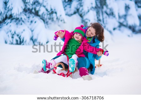 Young mother and little girl enjoying sleigh ride. Child sledding. Toddler kid riding sledge. Children play outdoors in snow. Kids sled in snowy park. Outdoor winter fun for family Christmas vacation.