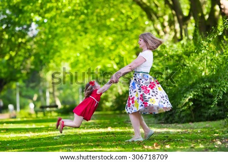 Family with kids playing in a park. Woman and little girl spin and dance in the garden. Grandmother and granddaughter play outdoors. Summer dress for mother and daughter. Active parents with children.