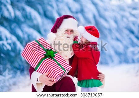 Santa Claus and children opening presents in snowy forest. Kids and father in Santa costume and beard open Christmas gifts. Little girl helping with present sack. Xmas, snow and winter fun for family.