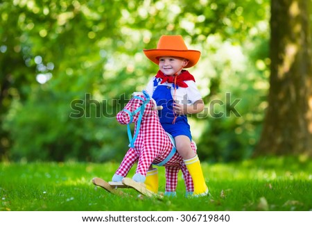 Little boy dressed up as cowboy playing with his toy rocking horse in a summer park. Kids play outdoors. Children in Halloween costumes at trick or treat. Toys for preschooler or toddler child.