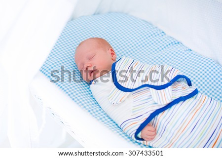 Adorable newborn baby sleeping swaddled in white bed. New born boy taking a nap in blue crib. Kids sleep. Swaddling for infants. Little kid wrapped in warm blanket relaxing in crib with canopy.