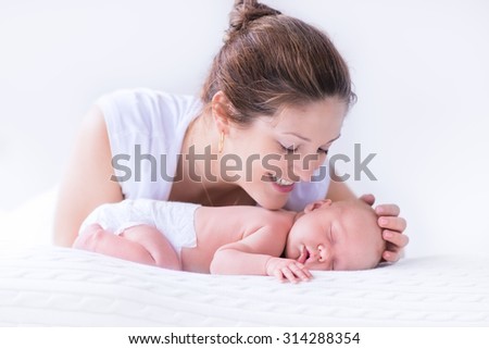 Young mother hugging her newborn child. Mom nursing baby. Woman and new born boy relax in a white bedroom. Family at home. Love, trust and tenderness concept. Bedding and textile for nursery.