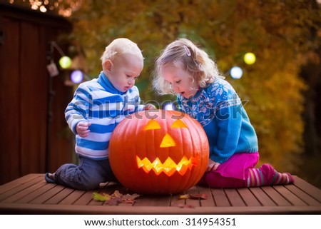 Little girl and boy carving pumpkin at Halloween. Dressed up children trick or treating. Kids trick or treat. Child in witch costume playing in autumn park. Toddler kid with jack-o-lantern.