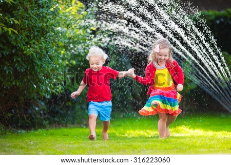 Child playing with garden sprinkler. Preschooler kid run and jump. Summer outdoor water fun in the backyard. Children play with hose watering flowers. Kids splash on sunny day. Selective focus on boy.