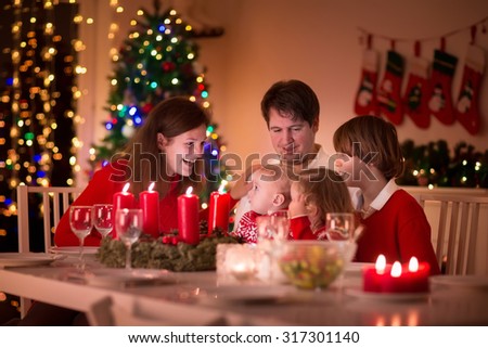 Big family with three children celebrating Christmas at home. Festive dinner at fireplace and Xmas tree. Parent and kids eating at fire place in decorated room. Child lighting advent wreath candle