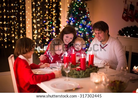 Big family with three children celebrating Christmas at home. Festive dinner at fireplace and Xmas tree. Parent and kids eating at fire place in decorated room. Child lighting advent wreath candle