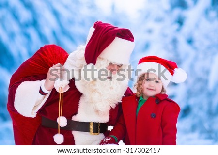 Santa Claus and children opening presents in snowy forest. Kids and father in Santa costume and beard open Christmas gifts. Little girl helping with present sack. Xmas, snow and winter fun for family