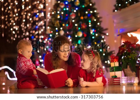 Family on Christmas eve at fireplace. Mother and little kids opening Xmas presents. Children with gift boxes. Living room with traditional fire place and decorated tree. Cozy winter evening at home