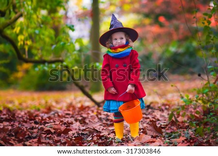 Little girl in witch costume playing in autumn park. Child having fun at Halloween trick or treat. Kids trick or treating.  Toddler kid with jack-o-lantern. Children with candy bucket in fall forest