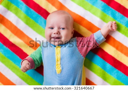 Smiling baby boy in bed. Laughing child on a colorful blanket. Children sleep. Bedding for kids. Newborn napping in bed. Healthy little new born kid shortly after birth. Clothing for kids.