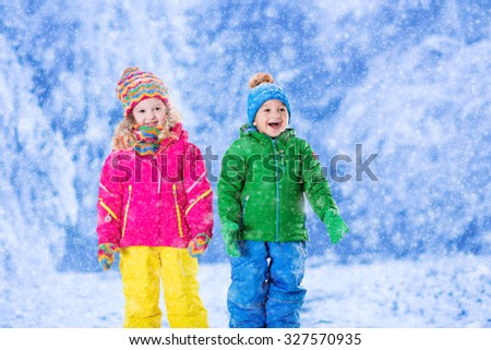 Little girl and boy in colorful hat catching snowflakes in winter park on Christmas eve. Ski vacation for family with children. Kids play outdoor in snowy forest. Children catch snow flake on Xmas