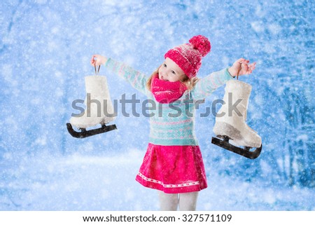 Happy laughing little girl having fun ice skating in snowy park. Winter sport and outdoor activity for family with children on Christmas vacation. Funny kid playing with snow. Child holding skates