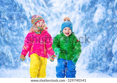 Little girl and boy in colorful hat catching snowflakes in winter park on Christmas eve. Ski vacation for family with children. Kids play outdoor in snowy forest. Children catch snow flake on Xmas.
