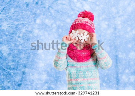 Little girl in blue knitted sweater and pink hat catching snowflakes in winter park. Kids play outdoor in snowy forest. Children catch snow flakes. Toddler kid playing outside in snow storm.
