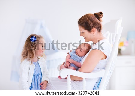 Little sister hugging her newborn brother. Toddler kid meeting new sibling. Mother and new born baby boy relax in a white bedroom. Family with children at home. Love, trust and tenderness concept.