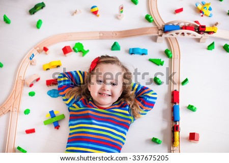 Child playing with wooden train, rails and cars. Toy railroad for kids. Educational toys for preschool and kindergarten children. Little girl at daycare. View from above, kid playing on the floor.