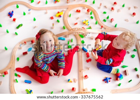 Children playing with wooden train. Toy railroad. Toddler kid and baby play with blocks, trains and cars. Educational toys for preschool and kindergarten child. View from above, kids on the floor.