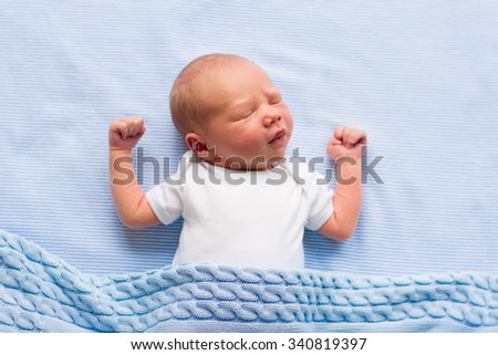 Newborn baby boy in bed. New born child sleeping under a blue knitted blanket. Children sleep. Bedding for kids. Infant napping in bed. Healthy little kid shortly after birth. Cable knit textile.