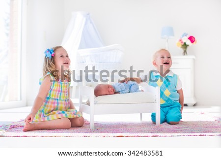 Cute little boy and girl kissing newborn brother. Toddler kids meet new born sibling at home. Infant sleeping in toy bed in white nursery. Kids playing and bonding. Children with small age difference.