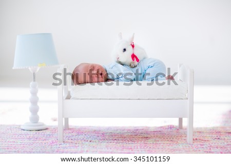 Adorable new born kid sleeping in a white toy bed with real rabbit. Nursery for newborn baby. Cute boy taking a nap in sunny bedroom with his bunny. Family with children and pets. Child and animal.