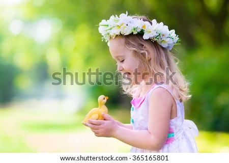 Little girl having fun on Easter egg hunt. Kid in flower crown playing with toy duck or chicken. Children searching for eggs in the garden. Toddler kids outdoor. Happy child laughing and smiling.