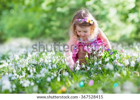 Little girl having fun on Easter egg hunt. Kids in blooming spring garden with crocus and snowdrop flowers. Children searching for eggs in the garden. Child putting colorful pastel eggs in a basket.