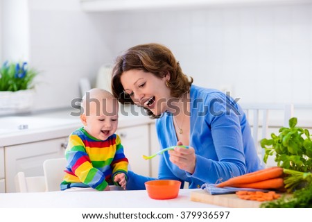 Mother feeding child. First solid food for young kid. Fresh organic carrot for vegetable lunch. Baby weaning. Mom and little boy eat vegetables. Healthy nutrition for children. Parents feed kids.