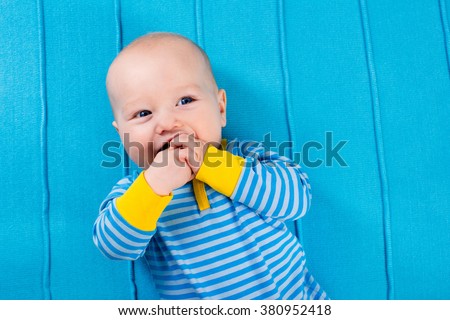 Cute baby on blue knitted blanket. Teething infant playing with colorful toy. Little boy in bed after nap. Bedding and textile for nursery and young children. Kids sleep wear. Newborn child at home.