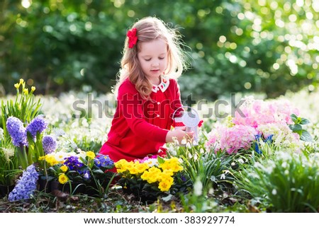 Child planting spring flowers in sunny garden. Little girl gardener plants hyacinth, daffodil, snowdrop in flower bed. Gardening tools and water can for kids. Family with children work in the backyard