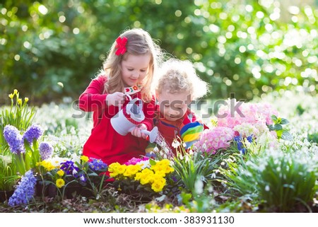 Children planting spring flowers in sunny garden. Little boy and girl gardener plant hyacinth, daffodil, snowdrop in flower bed. Gardening tools and water can for kids. Family working in the backyard.
