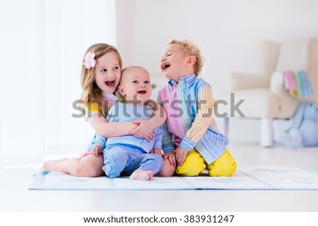 Group of three kids playing in a white bedroom. Children play at home. Preschooler girl, toddler boy and baby in nursery. Happy little brothers and sister bonding having fun together. Siblings love.