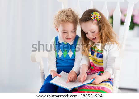 Kids read a book. Children reading books in white chair. Toddler kid and preschooler child doing homework. Little boy and girl study at home after kindergarten. Brother and sister play and laugh.