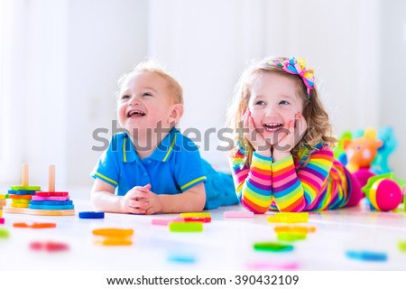 Kids playing with wooden toys. Two children, toddler girl and funny baby boy, playing with wooden toy blocks, building towers at home or day care. Educational child toys for preschool and kindergarten
