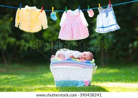 Newborn baby on a pile of clean dry towels. New born child after bath in a towel. Family washing clothes. Kids wear hanging on a line outdoors in summer garden. Infant apparel, textile for children.