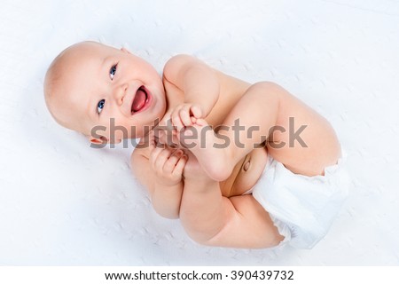 Funny little baby wearing a diaper playing on a white knitted blanket in a sunny nursery. Child after bath or shower on a fresh towel. Infant nappy change and skin care. Cute kid playing with his feet