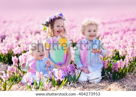 Three children playing in beautiful hyacinth flower field. Little girl, toddler boy and baby play in sunny summer garden with purple flowers. Kids having fun outdoors. Brothers and sister together.