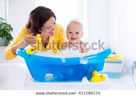 Happy baby taking a bath playing with foam bubbles. Mother washing little boy. Young child in a bathtub. Smiling kids in bathroom with toy duck. Mom bathing infant. Parent and kid play with water.