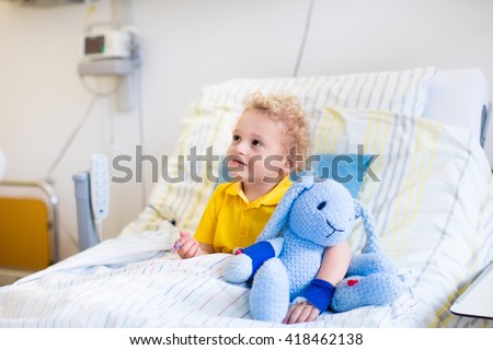 Little boy playing with his toy in bed in hospital room. Child with IV tube and pulse oximeter in modern clinic. Kid recovering from sickness. Post operative care at children station. Kids health care