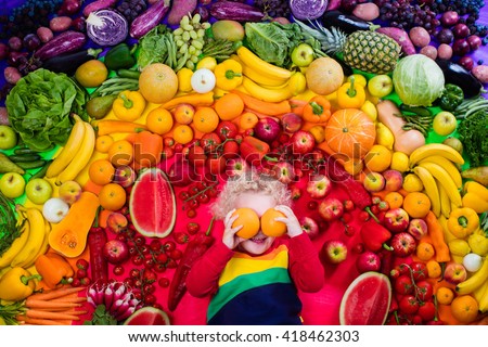 Little boy with variety of fruit and vegetable. Colorful rainbow of raw fresh fruits and vegetables. Child eating healthy snack. Vegetarian nutrition for kids. Vitamins for children. View from above.