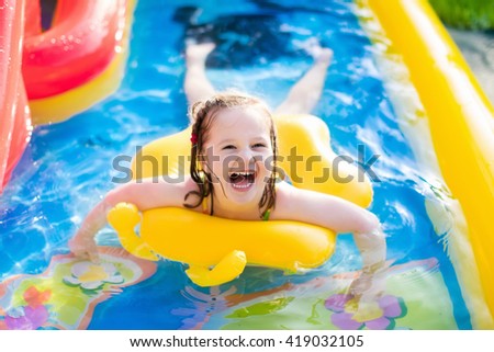 Children playing in inflatable baby pool. Kids swim and splash in colorful garden play center. Happy little girl playing with water toys on hot summer day. Family having fun outdoors in the backyard.