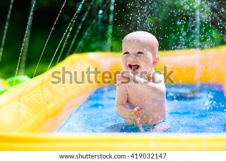 Children playing in inflatable baby pool. Kids swim and splash in colorful garden play center. Happy little boy playing with water toys on hot summer day. Family having fun outdoors in the backyard.