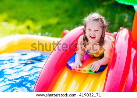 Children playing in inflatable baby pool. Kids swim and splash in colorful garden play center. Happy little girl playing with water toys on hot summer day. Family having fun outdoors in the backyard.