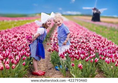 Happy Dutch children playing in blooming tulip flowers field.  Boy and girl wearing traditional national costume, wooden clogs and hat play with tulips next to a windmill in Holland, Netherlands