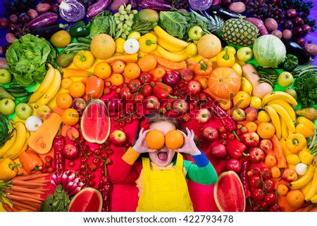 Little girl with variety of fruit and vegetable. Colorful rainbow of raw fresh fruits and vegetables. Child eating healthy snack. Vegetarian nutrition for kids. Vitamins for children. View from above.