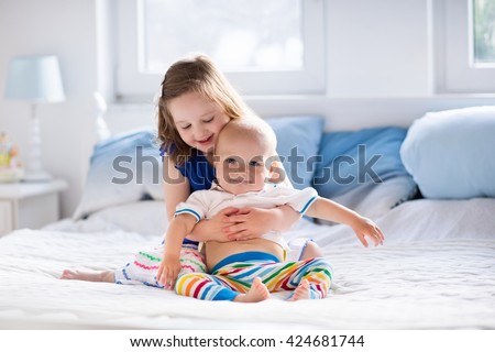 Little girl and baby boy, brother and sister playing in parents bed. Family with children in the morning. Kids play in white bedroom. Nursery crib bedding and textile for young child. Siblings love.