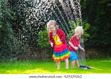 Child playing with garden sprinkler. Preschooler kid running and jumping. Summer outdoor water fun in the backyard. Children play with hose watering flowers. Kids run and splash on hot sunny day.